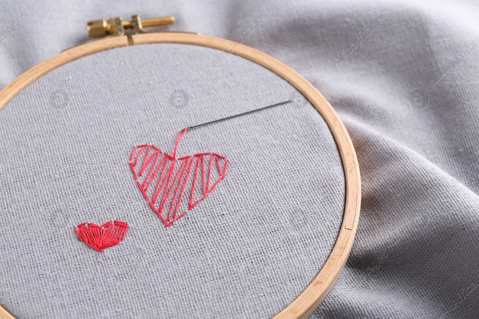 Photo of Embroidered red hearts and needle on light grey cloth, closeup