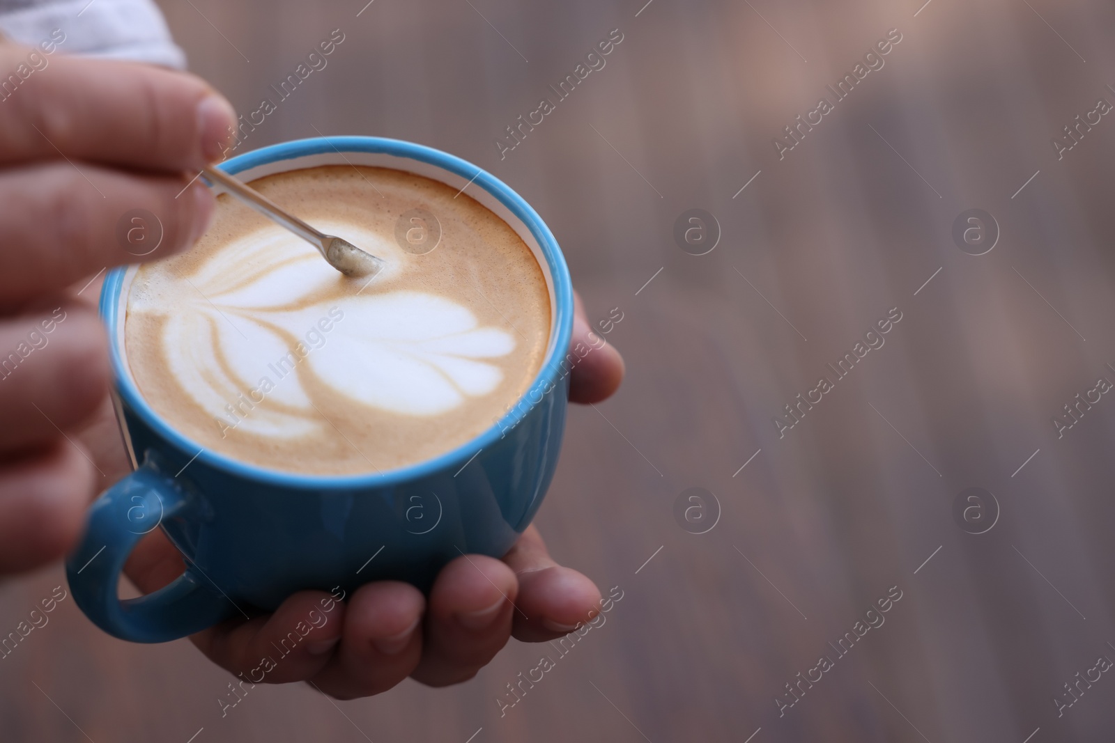 Photo of Barista creating pattern in cup of coffee on blurred background, closeup. Space for text