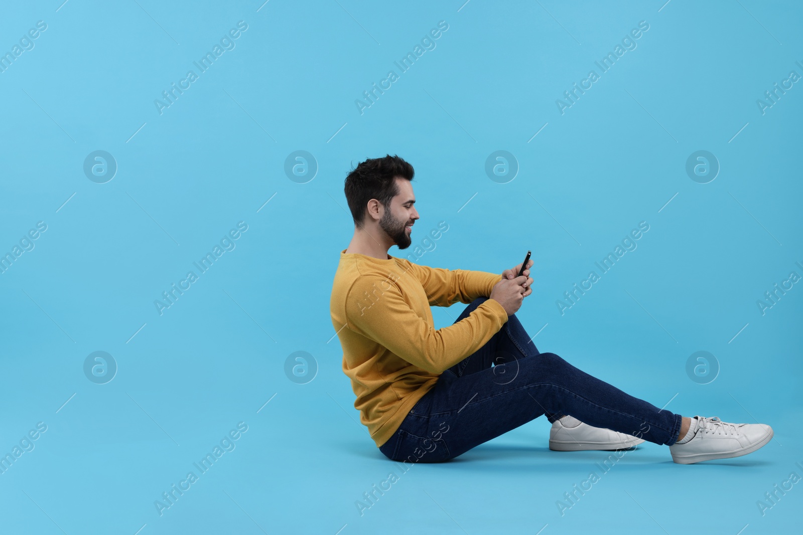 Photo of Handsome young man using smartphone on light blue background, space for text