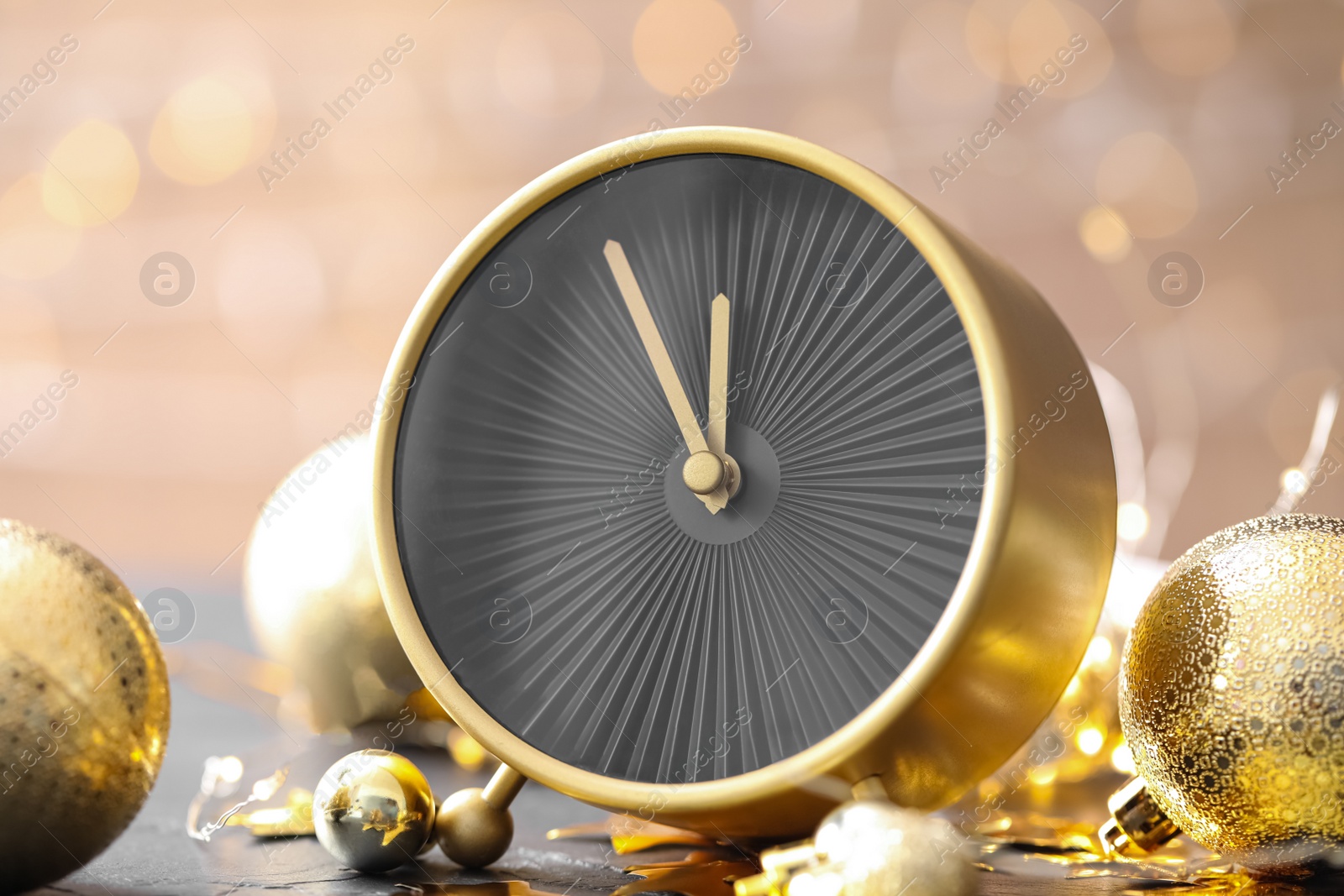 Photo of Stylish clock with decor on black table against blurred Christmas lights, closeup. New Year countdown