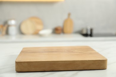 Wooden cutting board on white table in kitchen, closeup. Space for text