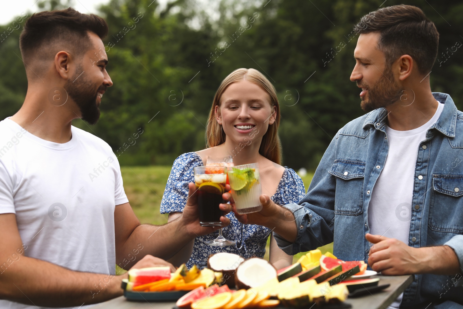 Photo of Happy friends clinking glasses with cocktails at table outdoors