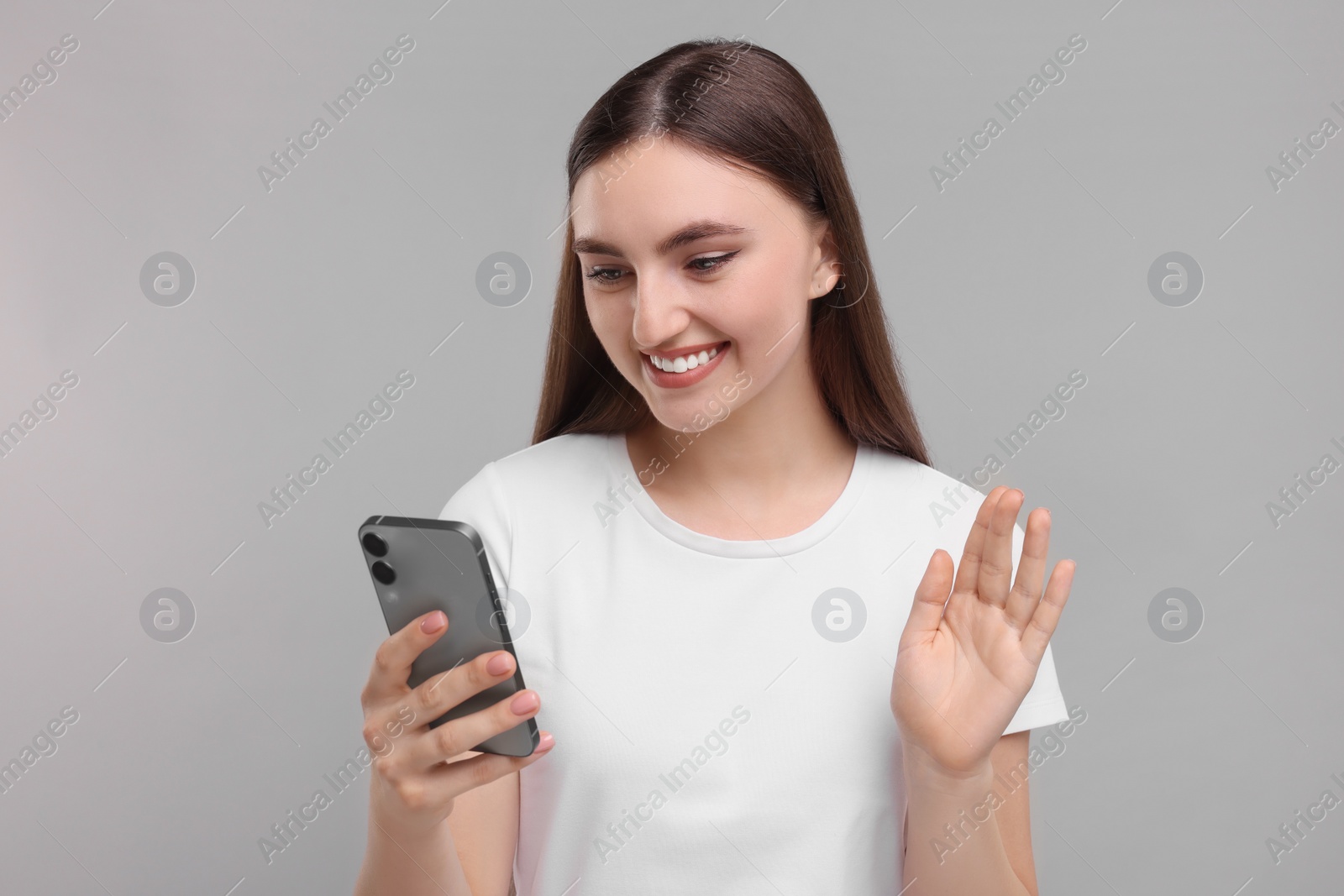 Photo of Smiling woman having videochat by smartphone on light grey background