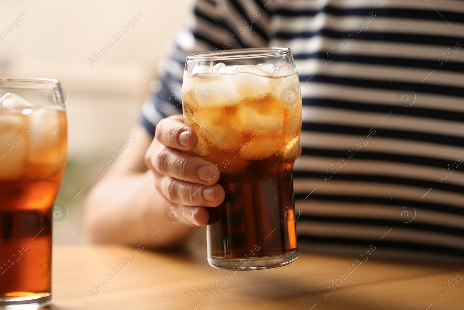 Photo of Woman holding glass of cola with ice at table, closeup