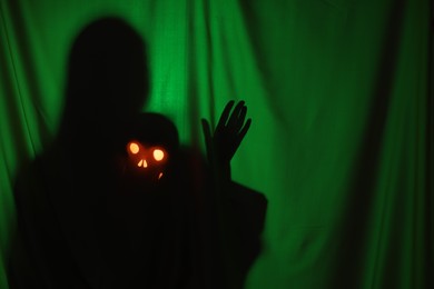 Silhouette of creepy ghost with skull behind dark green cloth, space for text