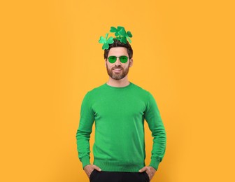 Image of St. Patrick's day party. Man with green sunglasses and clover headband on golden background
