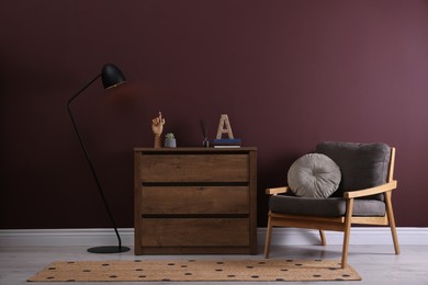 Photo of Elegant room interior with stylish chest of drawers, floor lamp and comfortable armchair near brown wall