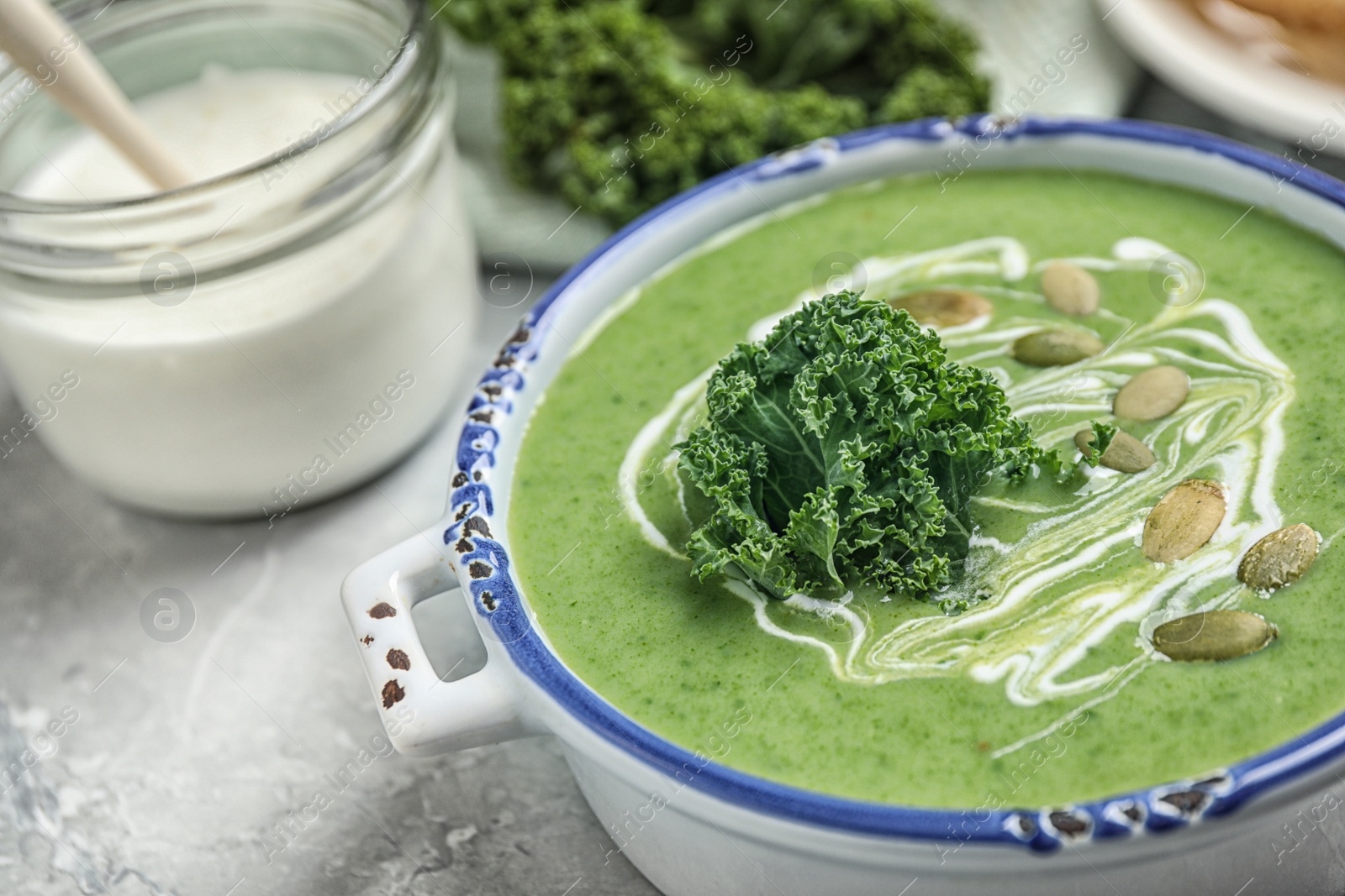 Photo of Tasty kale soup with pumpkin seeds on light grey marble table, closeup