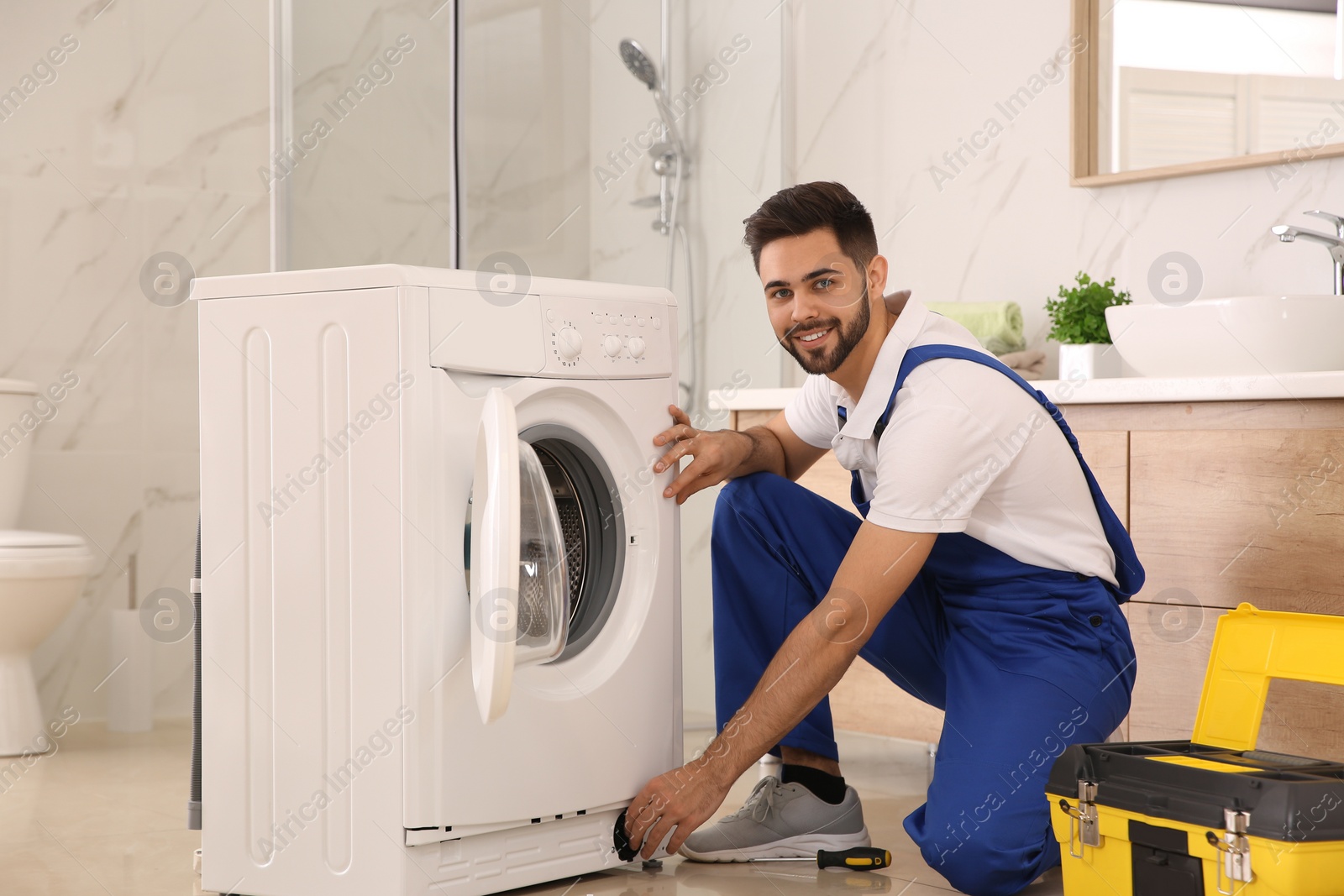 Photo of Professional plumber repairing washing machine in bathroom