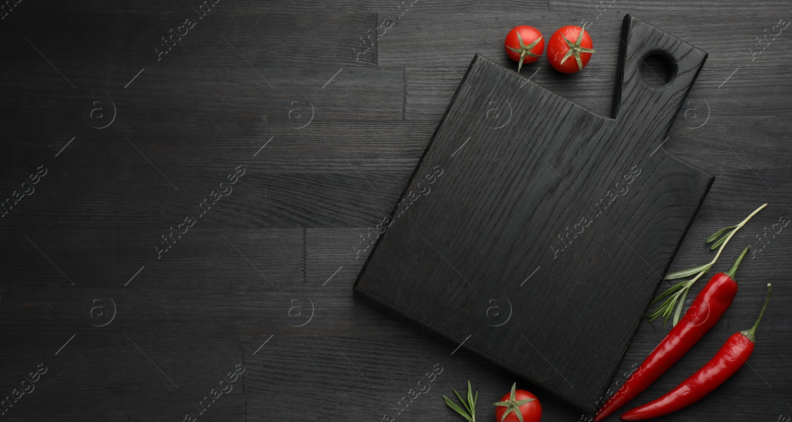 Photo of Cutting board, rosemary, chili peppers and tomatoes on black wooden table, flat lay. Space for text