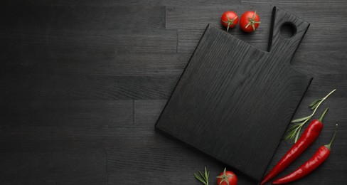 Photo of Cutting board, rosemary, chili peppers and tomatoes on black wooden table, flat lay. Space for text