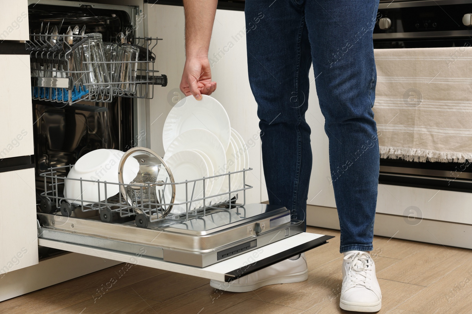 Photo of Man loading dishwasher with plates indoors, closeup