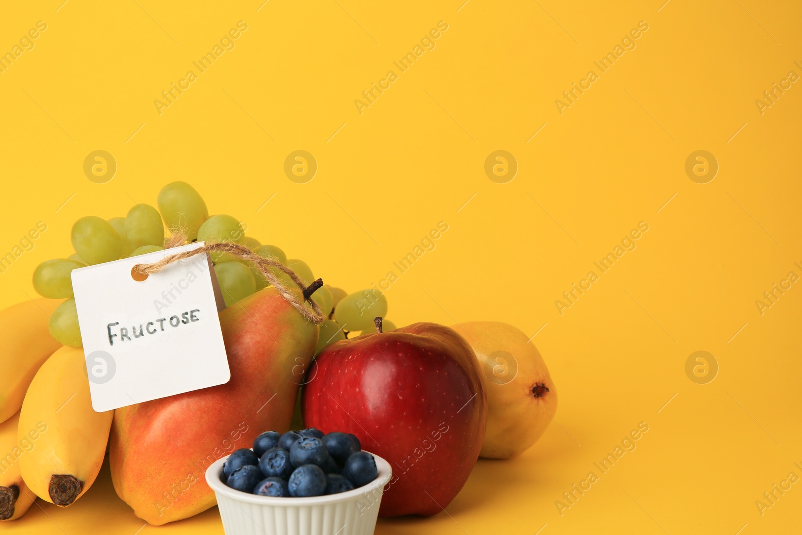 Photo of Card with word Fructose, delicious ripe fruits and blueberries on yellow background, space for text