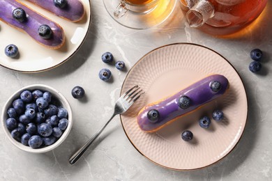 Photo of Tasty glazed eclairs with blueberries on grey marble table, flat lay