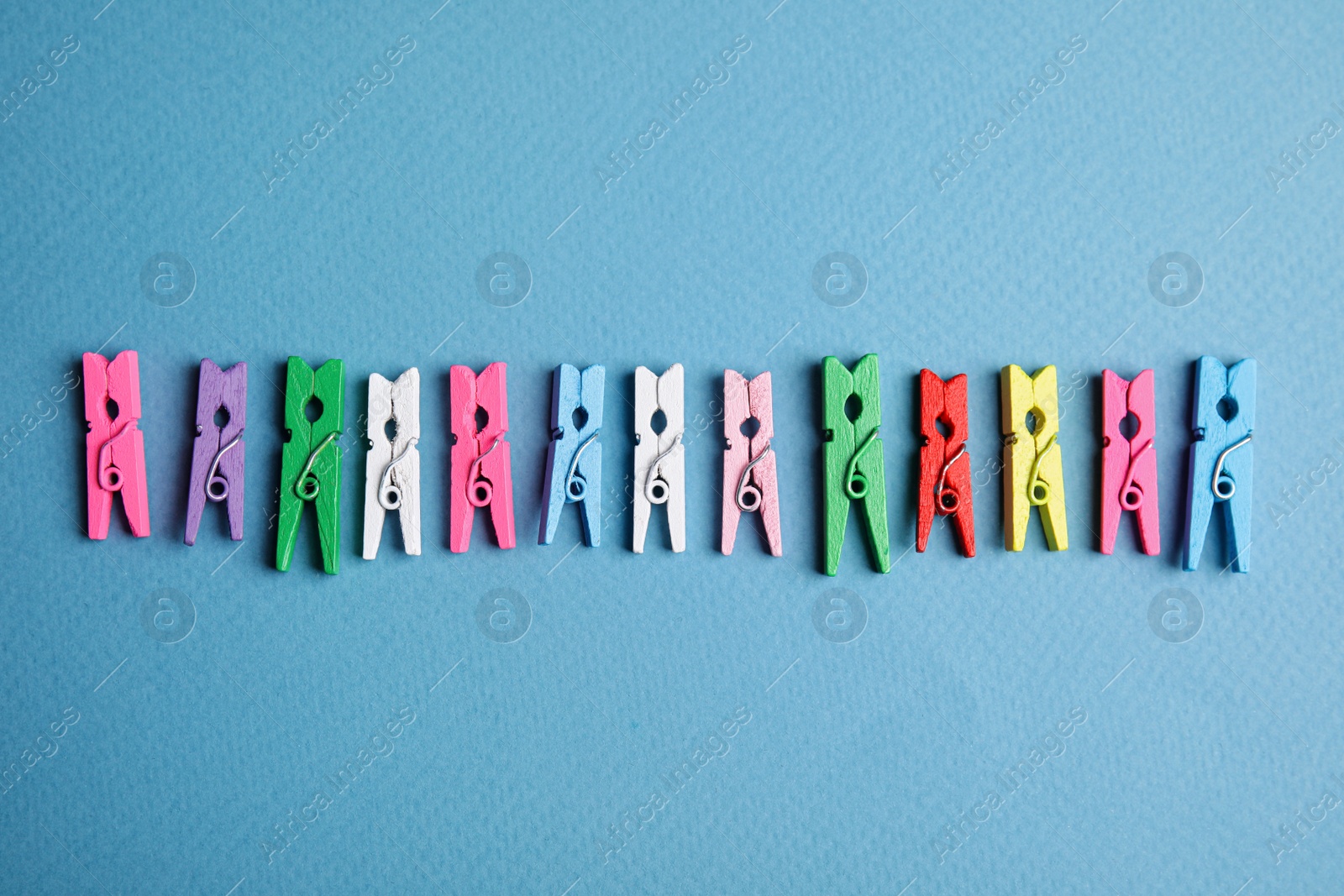 Photo of Many colorful wooden clothespins on light blue background, flat lay