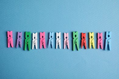 Photo of Many colorful wooden clothespins on light blue background, flat lay