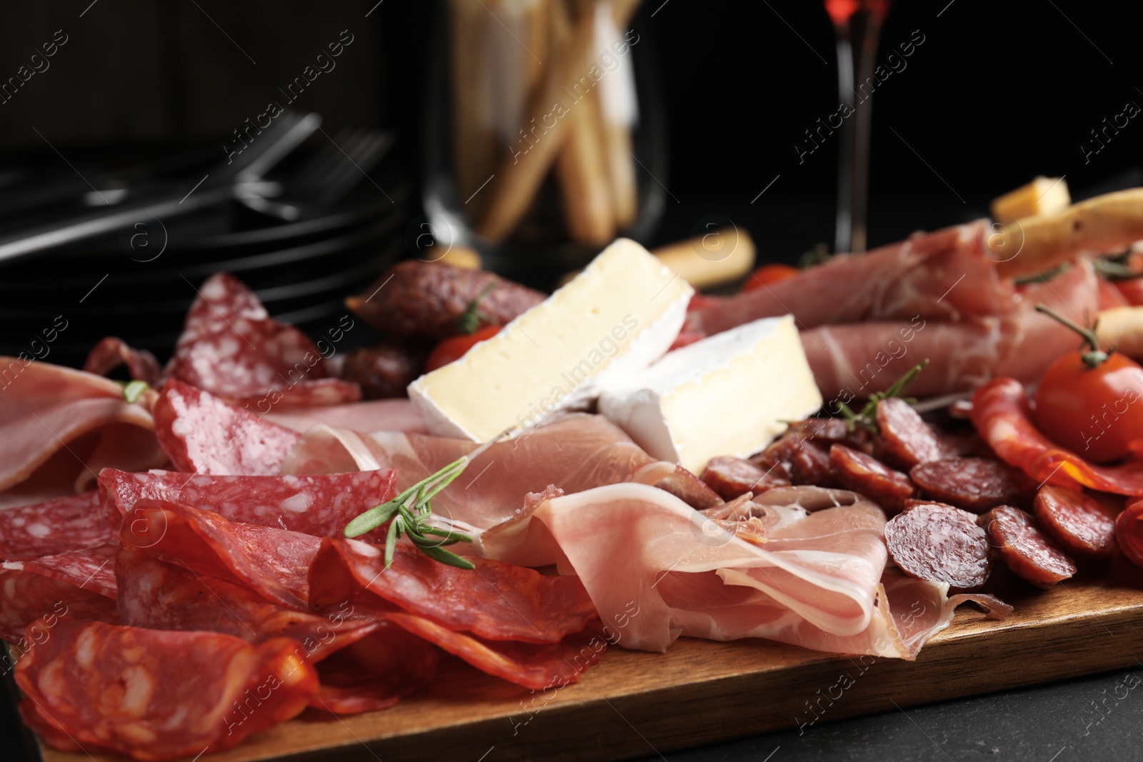 Photo of Tasty prosciutto with other delicacies served on black table, closeup