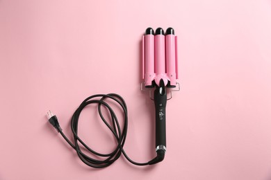 Photo of Modern triple curling hair iron on pink background, top view