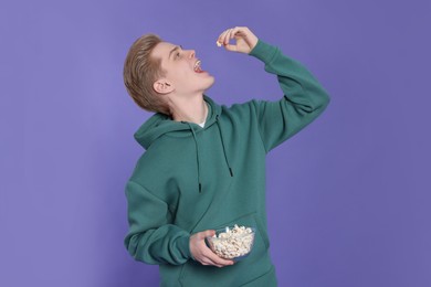 Teenage boy eating delicious popcorn on purple background