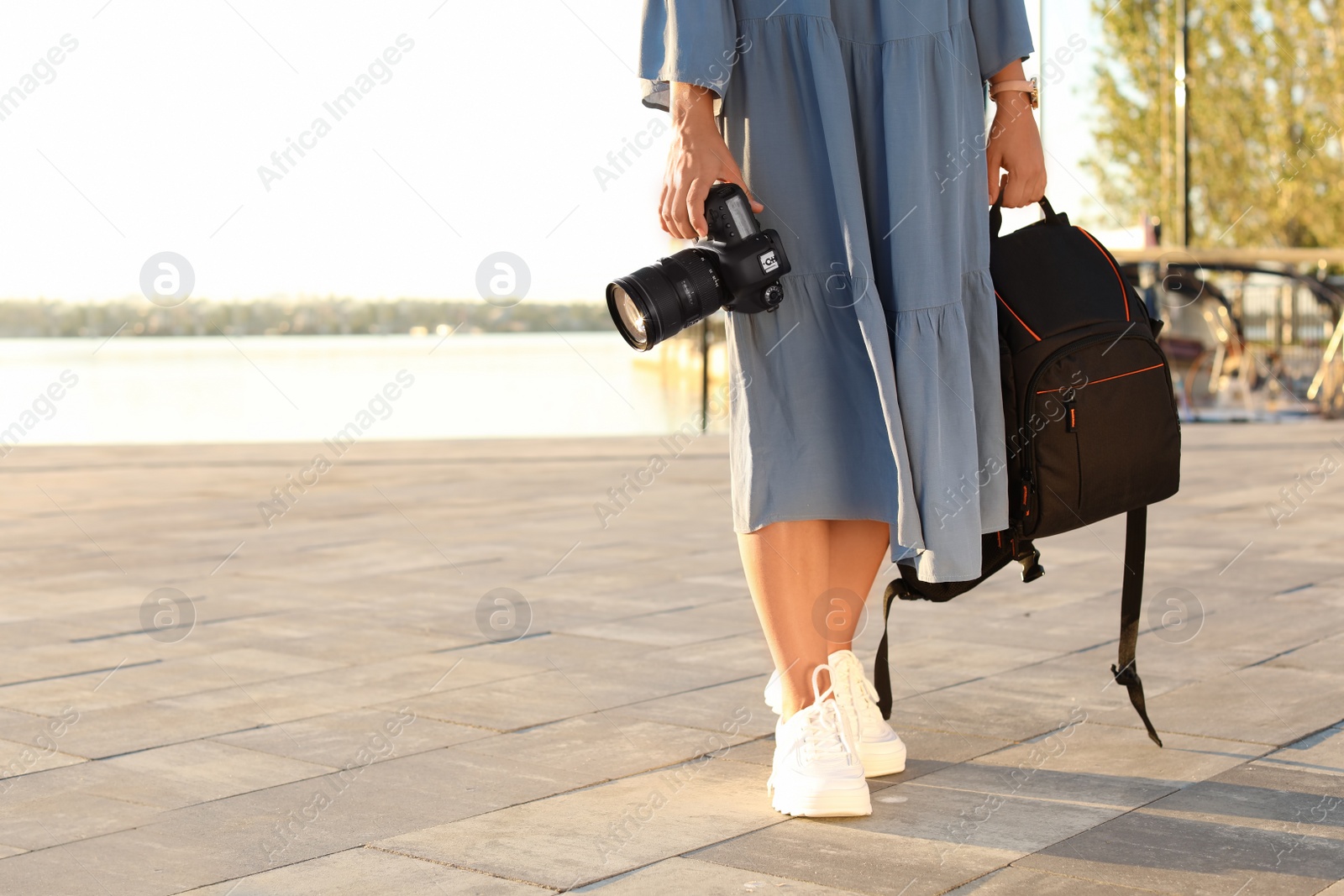 Photo of Young female photographer holding professional camera and backpack at pier. Space for text