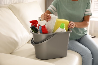 Photo of Woman holding bucket with cleaning supplies in living room, closeup