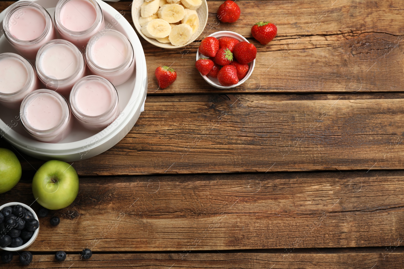 Photo of Modern yogurt maker with full jars and different fruits on wooden table, flat lay. Space for text