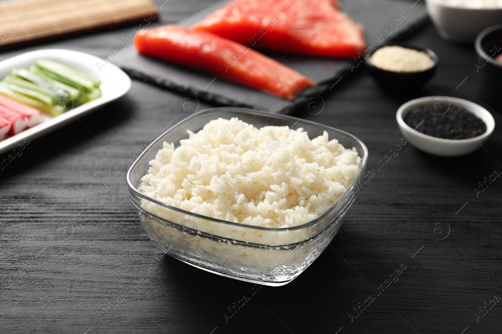Photo of Cooked rice for sushi in bowl on black wooden table, closeup
