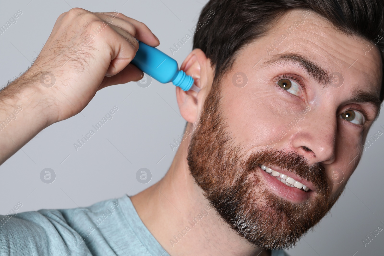Photo of Man using ear drops on grey background, closeup