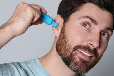 Man using ear drops on grey background, closeup