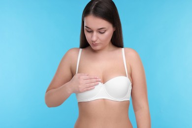 Mammology. Woman in bra doing breast self-examination on light blue background