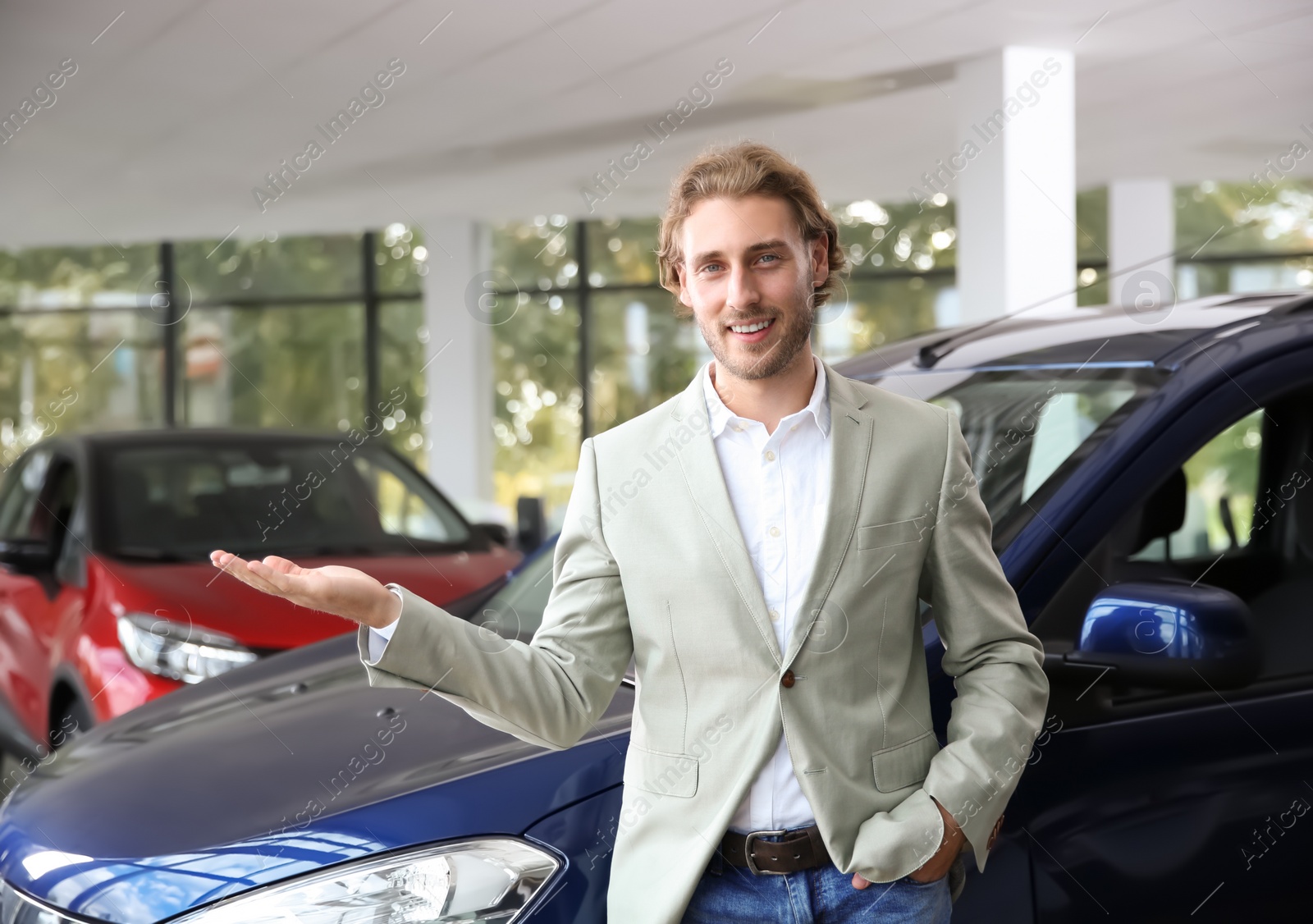 Photo of Young man near new car in modern auto dealership