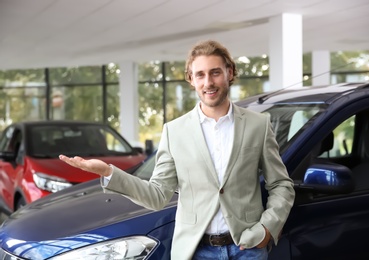 Young man near new car in modern auto dealership