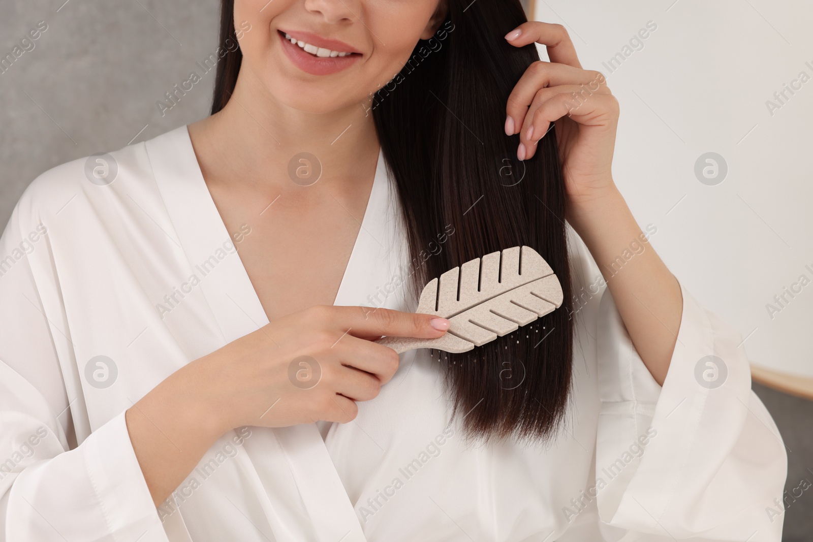 Photo of Young woman brushing her hair indoors, closeup