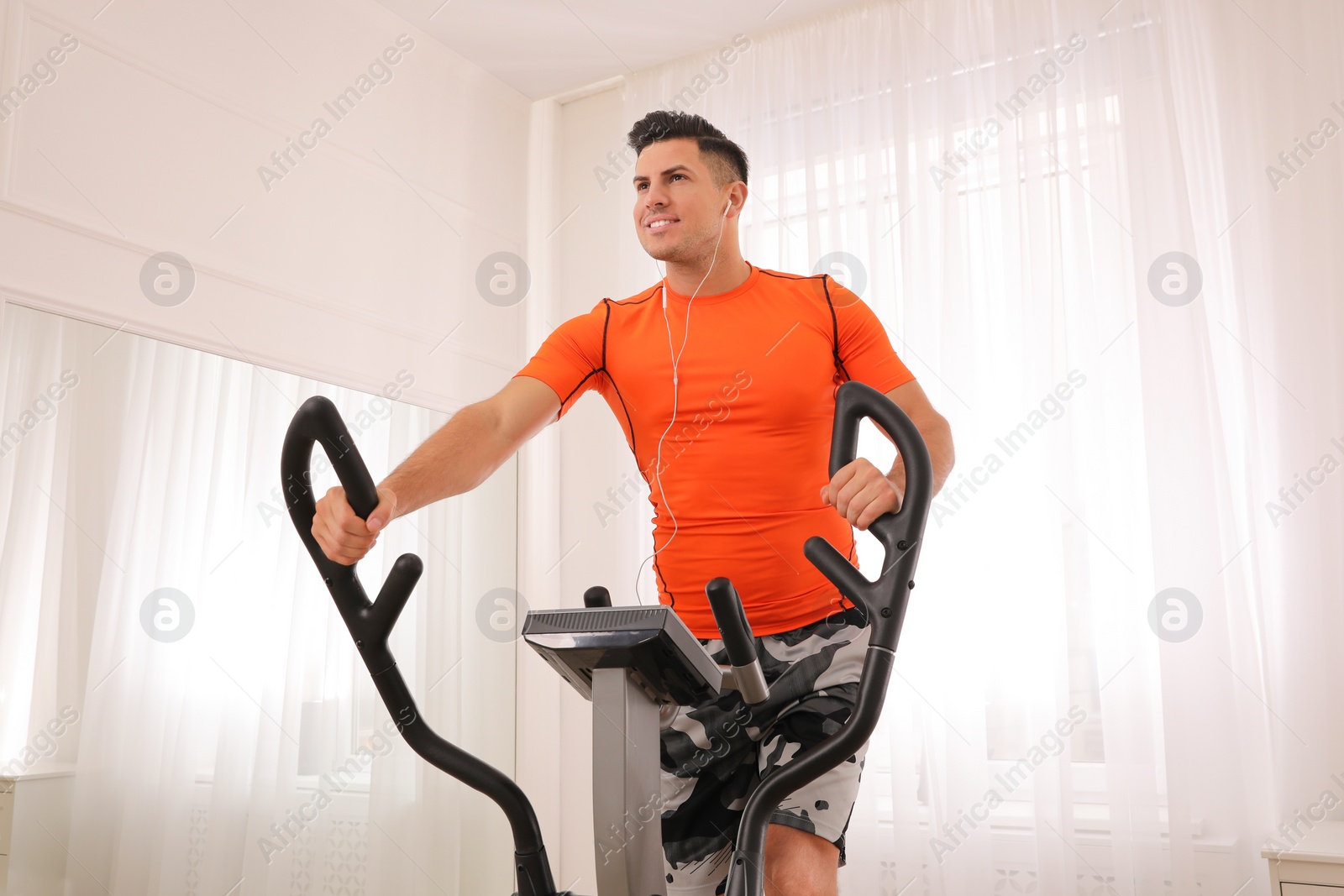 Photo of Man using modern elliptical machine at home