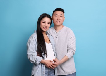 Pregnant woman and her husband on light blue background, space for text