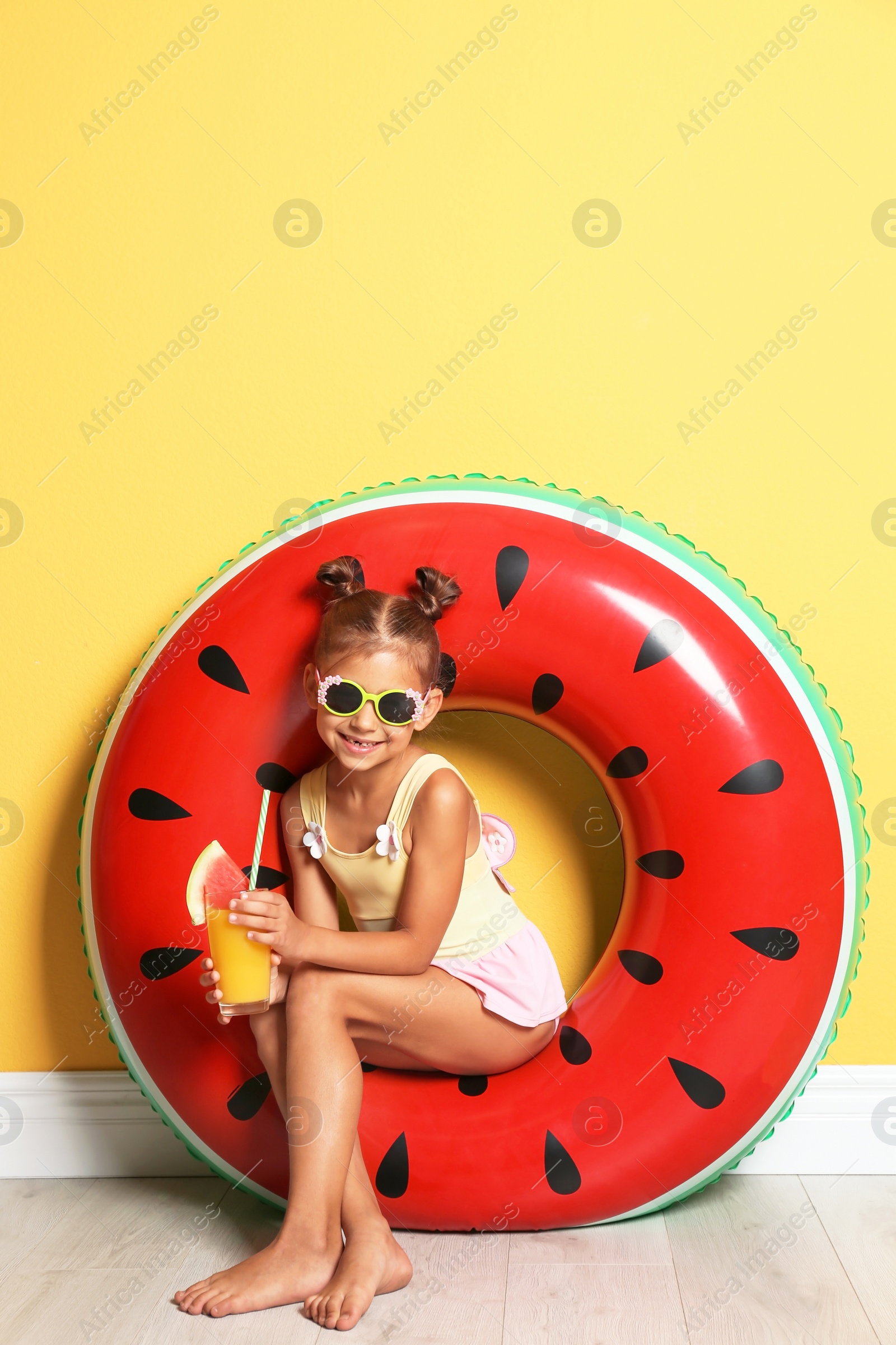 Photo of Cute little girl with inflatable ring and glass of cocktail near color wall