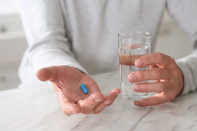 Photo of Senior man with pill and glass of water at table on blurred background, closeup