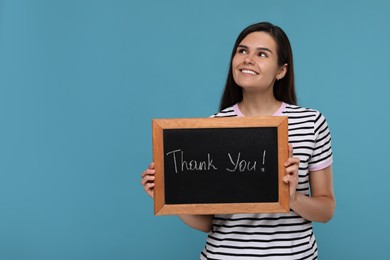 Photo of Happy woman holding small chalkboard with phrase Thank You on light blue background, space for text