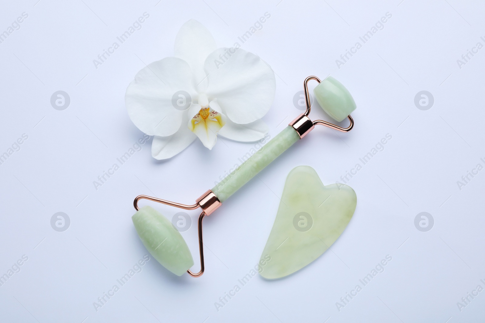 Photo of Gua sha stone, face roller and orchid flower on white background, flat lay