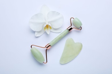 Photo of Gua sha stone, face roller and orchid flower on white background, flat lay