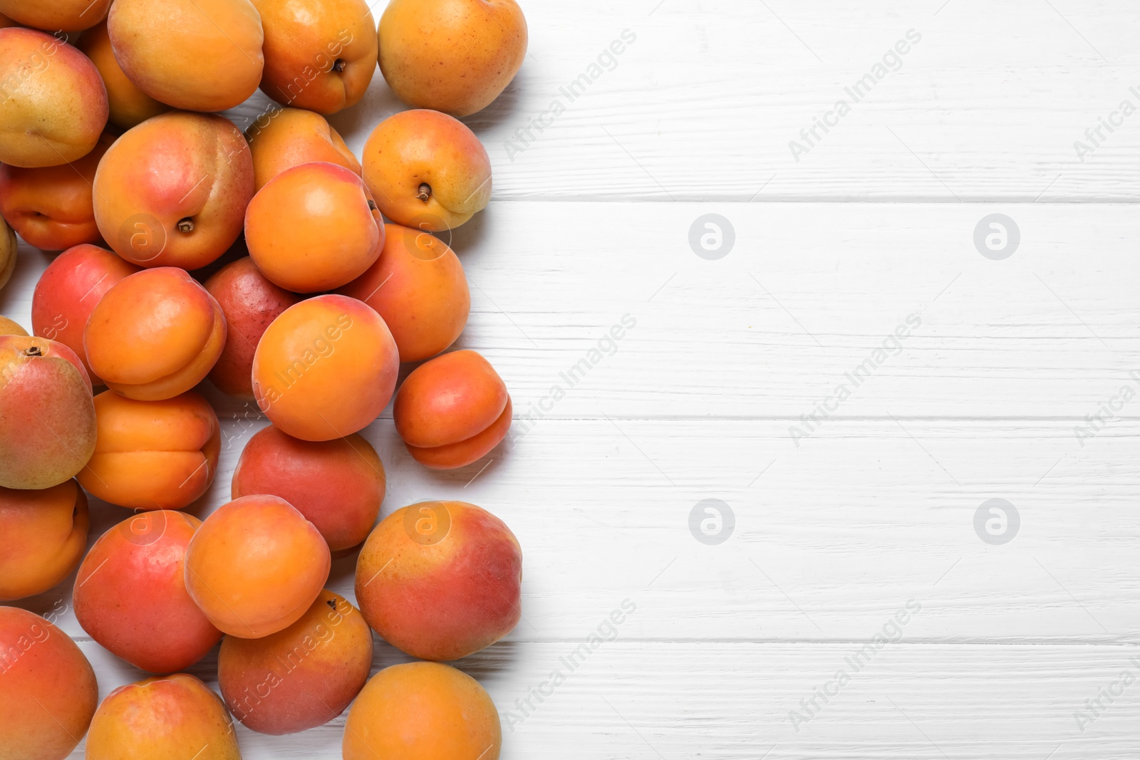 Photo of Delicious fresh ripe apricots on white wooden table, flat lay. Space for text