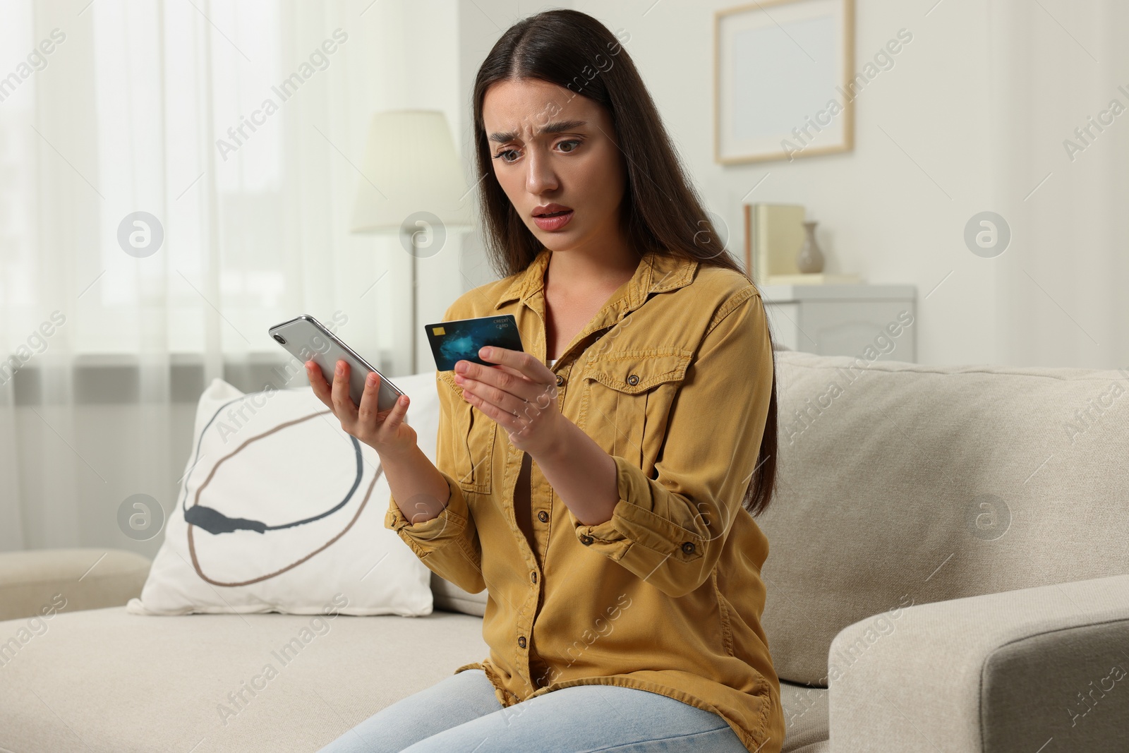 Photo of Shocked woman with credit card and smartphone at home. Be careful - fraud