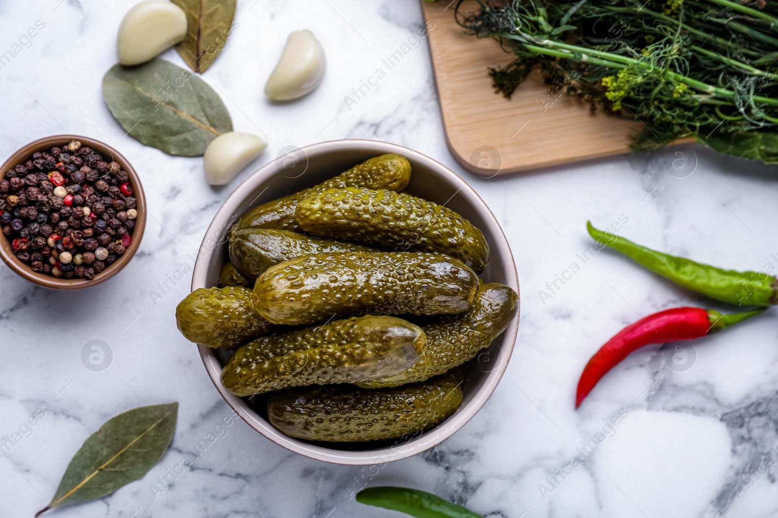 Photo of Bowl of pickled cucumbers and ingredients on white marble table, flat lay