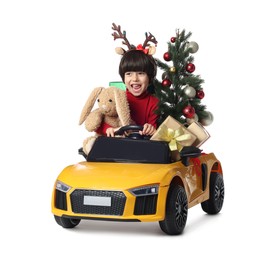 Photo of Cute little boy with Christmas tree, bunny toy and gift boxes driving children's car on white background