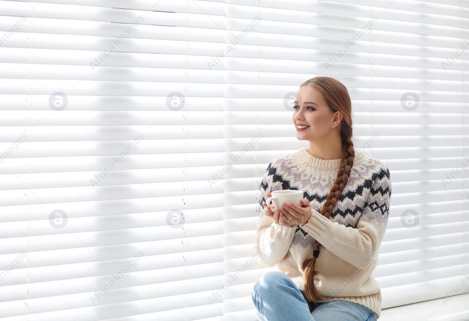 Photo of Young woman with hot drink near window at home