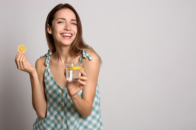 Photo of Young woman with glass of lemon water on light background. Space for text