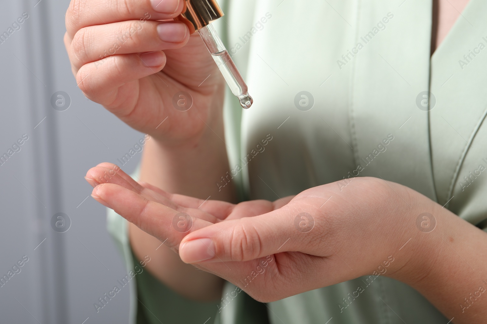 Photo of Woman applying cosmetic serum onto hand on grey background, closeup