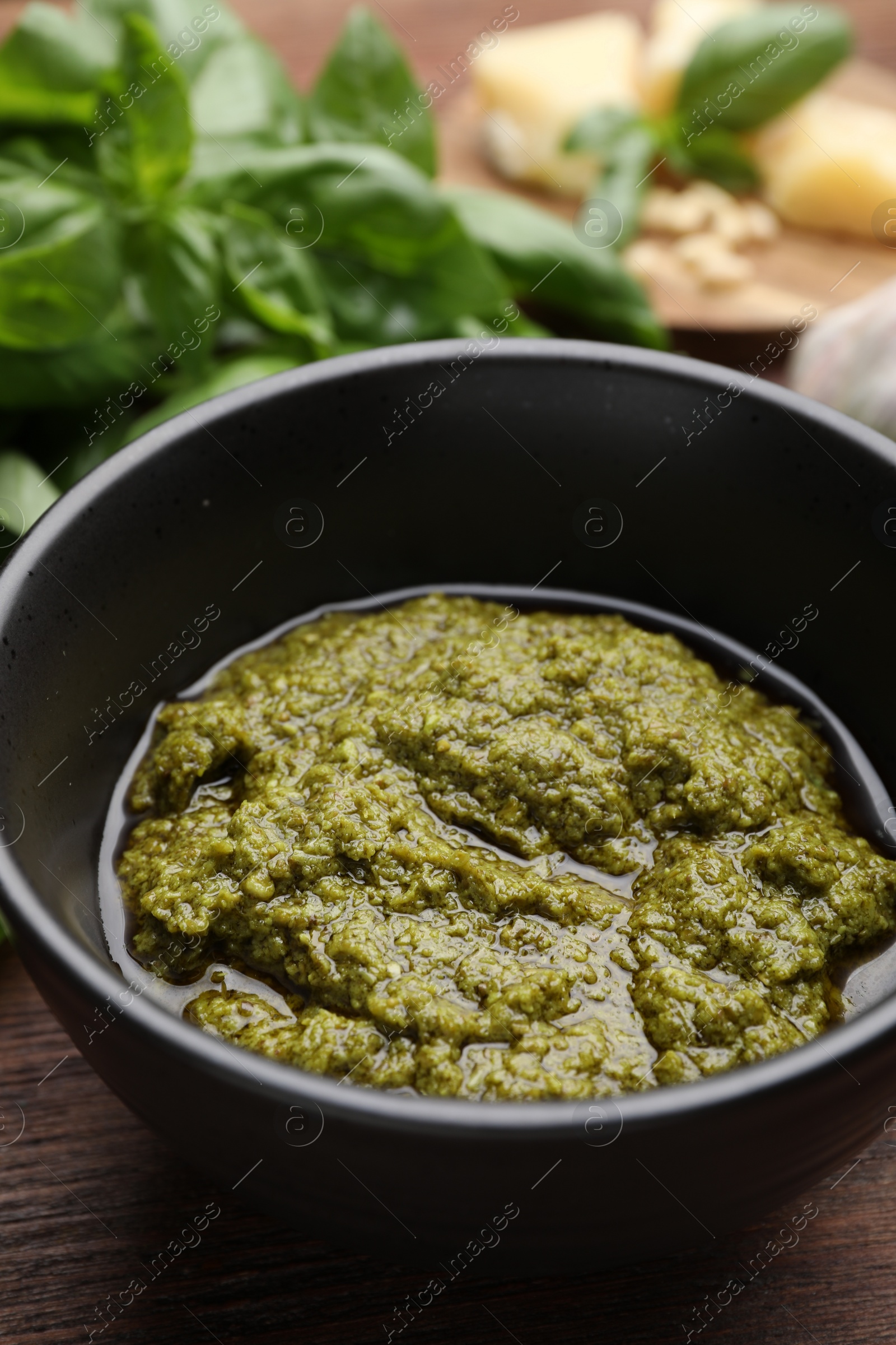 Photo of Tasty pesto sauce in bowl and basil on wooden table, closeup