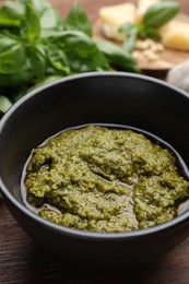 Tasty pesto sauce in bowl and basil on wooden table, closeup