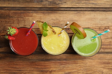 Delicious colorful juices in glasses on wooden table, flat lay